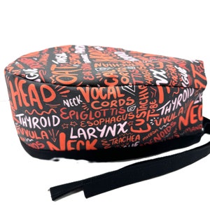 May include: Black scrub hat with a red and pink print of anatomical terms related to the head and neck. The hat has a black tie.