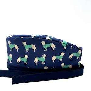 Może przedstawiać: Czapka chirurgiczna w kolorze granatowym z wzorem złotych retrieverów noszących zielone maski chirurgiczne. Czapka ma granatowy pasek.