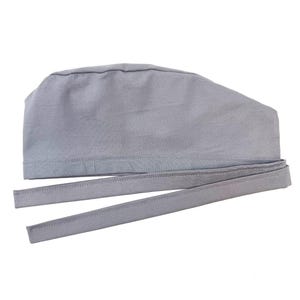 Op de afbeelding: Een lichtgrijze chirurgische muts met lange strikken. De muts is gemaakt van een zachte stof en heeft een eenvoudig, functioneel ontwerp. De strikken worden gebruikt om de muts vast te zetten.