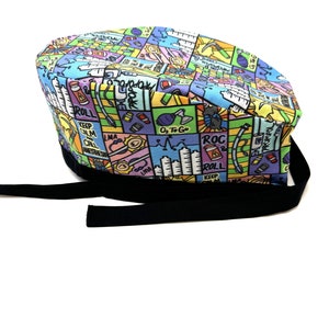 May include: A colorful surgical scrub hat with a black tie. The hat features a variety of medical-themed illustrations and text, including "Keep Calm and Roll On", "O₂ To Go", "ROC & Roll", and "LMA".