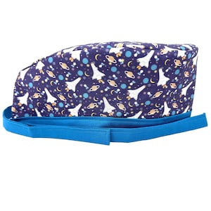 May include: A blue scrub hat with a space-themed print featuring rockets, planets, and stars. The hat has a blue tie.