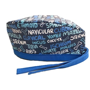 May include: Blue and white scrub hat with a pattern of anatomical terms and bone illustrations. The hat has a blue tie.