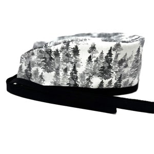 Op de afbeelding: Een witte scrubcap met een zwart-witte aquarelprint van bomen. De cap heeft een zwarte stropdas.