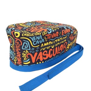 Może przedstawiać: Niebieski i czarny czepek chirurgiczny z kolorowym nadrukiem terminów medycznych, w tym "Naczyniowy", "Amputacja", "Aorta" i "Endarterektomia". Czepek ma niebieski sznurek.