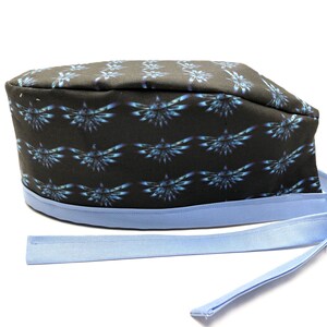 May include: Black scrub hat with a blue and black repeating pattern of a stylized bird. The hat has a light blue adjustable tie.