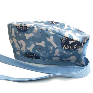 May include: Blue surgical scrub hat with a white bone pattern and the text "You We'll Fix 'Em" and "We'll Break 'Em".