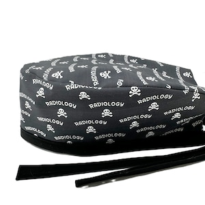 Może przedstawiać: Czarny chirurgiczny czepek z białym napisem "Radiology" i wzorem czaszki i skrzyżowanych piszczeli. Czepek ma czarne wiązania do mocowania. Ten czepek o tematyce medycznej jest przeznaczony dla pracowników służby zdrowia.