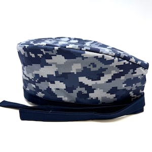 Op de afbeelding: Een blauwe en grijze camouflage scrub-muts met een donkerblauwe verstelbare strop.
