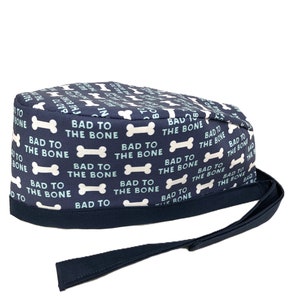 May include: A navy blue surgical scrub hat with a white bone pattern and the text "Bad to the Bone" repeated throughout. The hat has a navy blue tie.