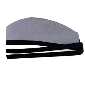 Op de afbeelding: Een grijze chirurgische scrubcap met zwarte banden. De cap is gemaakt van een zachte, duurzame stof en is ontworpen om te worden gedragen tijdens medische procedures. De zwarte banden zorgen voor een verstelbare en veilige pasvorm.