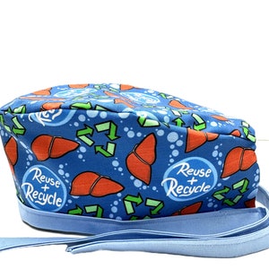 Może przedstawiać: Niebieski chirurgiczny czepek z wzorem czerwonych wątrob, zielonych strzałek recyklingu i białych bąbelków. Czepek ma niebieski sznurek i napis "Reuse + Recycle" nadrukowany na czepku.