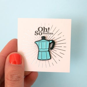 May include: A blue and black enamel pin featuring a traditional Italian coffee pot, with the text "Oh! So Italian" on a white card with a silver background.