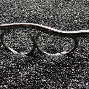 Könnte beinhalten: Ein polierter, silberfarbener Doppelring mit einer glatten, wellenförmigen horizontalen Stange, die zwei kreisförmige Ringe verbindet. Die metallische Oberfläche reflektiert das Licht und bildet eine elegante, durchgehende Form für zwei Finger.