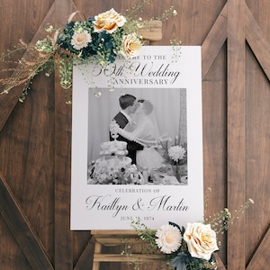 May include: A black and white photo of a couple kissing at their wedding. The photo is on a white sign with the text "Welcome to the 50th Wedding Anniversary Celebration of Kaitlyn & Martin June 18, 1974".