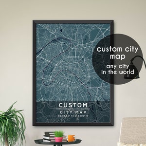 May include: A framed map of Paris, France, with a blue and white color scheme. The map shows the city's streets and landmarks. The text "CUSTOM CITY MAP 48.8564 N/2.3481 W" is printed below the map. The text "custom city map any city in the world" is printed in a circle in the upper right corner of the map.