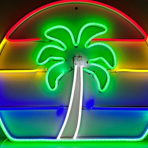 Puede incluir: Un letrero de neón con forma de puesta de sol con una palmera en el centro. El letrero está hecho de tubos de neón y tiene un fondo blanco. La puesta de sol está hecha de tubos de neón rojo, naranja, amarillo y azul. La palmera está hecha de tubos de neón verde.