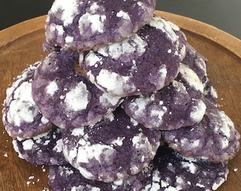 Puede incluir: Una pila de galletas moradas con azúcar en polvo blanco en la parte superior. Las galletas están dispuestas en forma de pirámide sobre una superficie de madera.