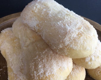 May include: A stack of five white, fluffy, bread rolls dusted with powdered sugar. The rolls are arranged in a pyramid shape on a wooden surface.