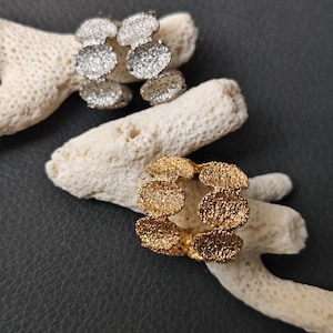May include: Two pairs of hoop earrings, one pair is gold and the other is silver. Both pairs are made of small, textured circles.
