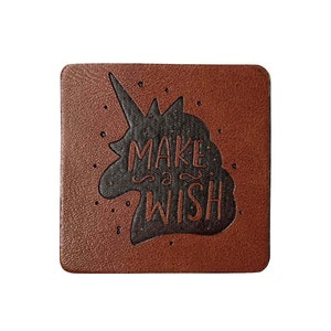 Puede incluir: Posavasos de cuero marrón con una silueta de unicornio negro y el texto "Make a Wish" en relieve.