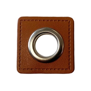Peut inclure: Un œillet en cuir marron avec un anneau en métal argenté. L'œillet a un bord cousu.