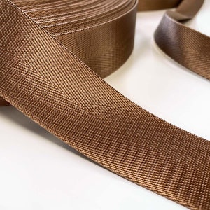 May include: A roll of brown woven ribbon with a subtle shimmer. The ribbon is flat and has a textured surface.