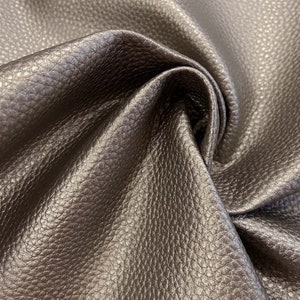 Könnte beinhalten: Nahaufnahme eines dunkelbraunen Ledermaterials mit einer strukturierten, genarbten Oberfläche. Das Leder ist gefaltet und zeigt die Tiefe und Flexibilität des Materials. Die Beleuchtung hebt die Farb- und Texturvariationen hervor.