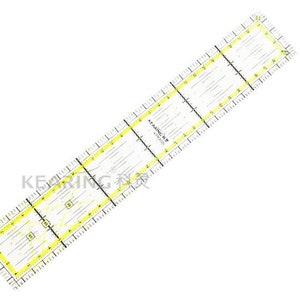 Può includere: Un righello in plastica trasparente con segni gialli. Il righello è diviso in sezioni con misure in pollici. Il righello è etichettato "A-Plastic 12" ruler".