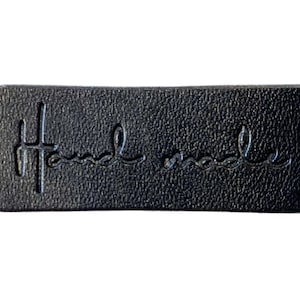 Könnte beinhalten: Schwarzes Leder-Etikett mit dem in Weiß geprägten Text "Hand made".