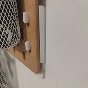 May include: A wooden pegboard with white accessories, including a ruler and hooks. A white mesh basket is partially visible on the left. The pegboard is mounted on a white wall.