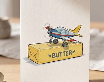 Puede incluir: Tarjeta de felicitación con una ilustración de dibujos animados de un avión pequeño posado sobre un bloque de mantequilla. El avión es azul, rojo y amarillo. La mantequilla es amarilla con la palabra "BUTTER".