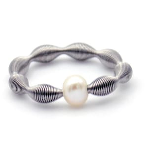 Puede incluir: Un anillo de plata con un diseño en espiral y una perla blanca en el centro.
