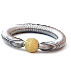 May include: A silver spring bracelet with a gold ball charm. The ball has a textured surface.