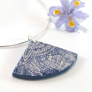 May include: A silver choker necklace with a blue and white ceramic pendant. The pendant is a half-circle shape and features a detailed, intricate design.