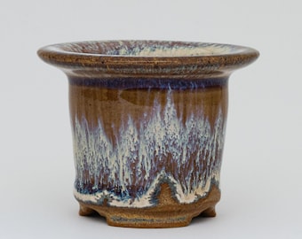 May include: A brown ceramic pot with a white and blue glaze. The pot has a wide rim and a flared base.