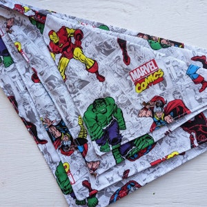May include: A stack of Marvel Comics themed bandanas. The bandanas feature comic book panels with characters like Iron Man, Hulk, and Thor. The Marvel Comics logo is visible. The bandanas are white with a gray comic book panel design.