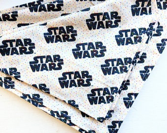 May include: White fabric with a repeating pattern of the words "STAR WARS" in navy blue. The text is filled with colorful dots. The fabric is folded, showing multiple layers.