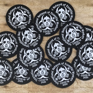 May include: A collection of black and white embroidered patches with a biohazard symbol and the text "International Network of Essential Workers COVID-19 2020".