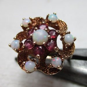 May include: A gold ring featuring a cluster of white opals and pink gemstones set in a swirling design.