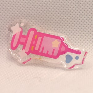 May include: A pink and white syringe with a star on the side, made of clear acrylic.