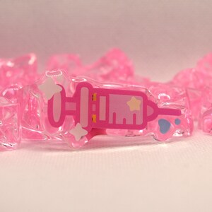 May include: A pink plastic syringe charm with a white star and a blue paw print. The charm is surrounded by pink plastic ice cubes.