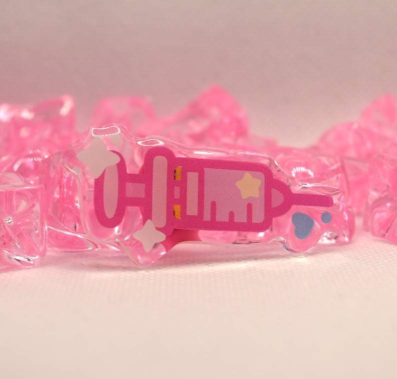 May include: A pink plastic syringe charm with a white star and a blue paw print. The charm is surrounded by pink plastic ice cubes.