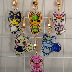 Może przedstawiać: Kolekcja akrylowych breloków do kluczy z różnymi postaciami zwierząt z kreskówek. Każdy brelok ma złote zapięcie. Postacie obejmują kota, wiewiórkę, niedźwiedzia i ośmiornicę, wszystkie o unikalnych wzorach i kolorach.