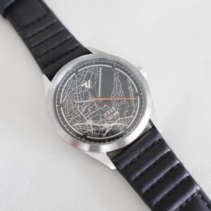 May include: A silver watch with a black leather band. The watch face features a map design with the text "YOUR TEXT HERE".
