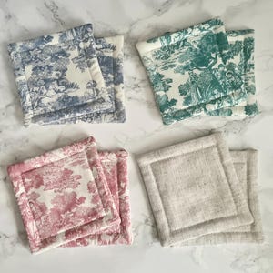 Può includere: Quattro set di sottobicchieri quadrati in tessuto. Un set presenta una scena pastorale blu e bianca, un altro una scena verde e bianca, un terzo una scena rosa e bianca e l'ultimo set è di colore lino neutro.