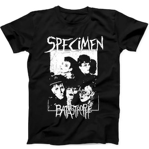 May include: A black short-sleeve t-shirt featuring a white graphic print of a band. The design includes the text SPECIMEN at the top and BATASTROPHE at the bottom, surrounding a high-contrast, grainy black and white photograph of four individuals.