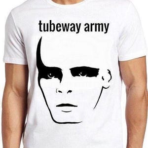 Pode incluir: Uma t-shirt branca de manga curta com uma impressão gráfica preta de um rosto humano com maquilhagem escura nos olhos e o texto tubeway army impresso em letras pretas acima do rosto. A peça tem gola redonda e um corte padrão.