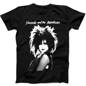Könnte beinhalten: Ein schwarzes Kurzarm-T-Shirt mit einem weißen Grafikdruck von Siouxsie Sioux mit voluminösem Haar und Netzärmeln. Der Text Siouxsie and the Banshees ist in einer weißen, stilisierten Schrift über dem Porträt auf der Vorderseite gedruckt.