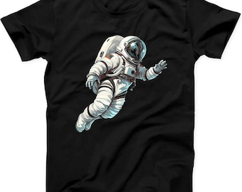 May include: A black short-sleeved t-shirt featuring a graphic illustration of an astronaut in a white space suit floating in space. The astronaut is depicted in a dynamic pose with a reflective helmet visor and detailed life support equipment.