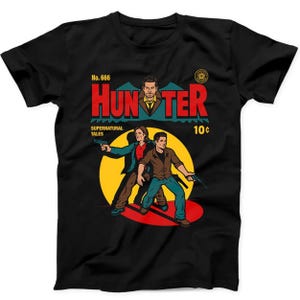 Puede incluir: Una camiseta negra de manga corta con un gráfico de portada de cómic. El diseño incluye el texto "No. 666", "HUNTER", "SUPERNATURAL TALES" y "10¢". Muestra tres figuras, dos de ellas sosteniendo pistolas, sobre un fondo de círculo amarillo.